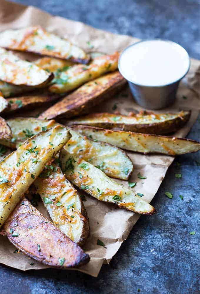 Baked potato wedges on brown paper beside a condiment cup of ranch dressing.