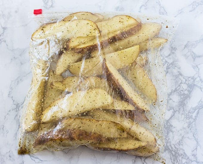 Raw potato wedges in a resealable bag with oil and seasonings.
