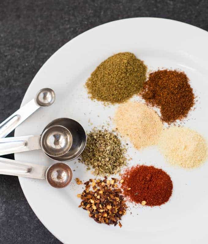Spices for tacos on a round white plate with a set of stainless measuring spoons.