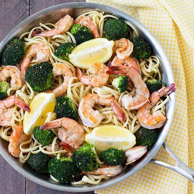 Overhead view of pasta topped with shrimp, broccoli and lemon wedges in a skillet. 