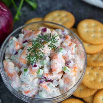 Shrimp Salad in a glass bowl beside round buttery crackers