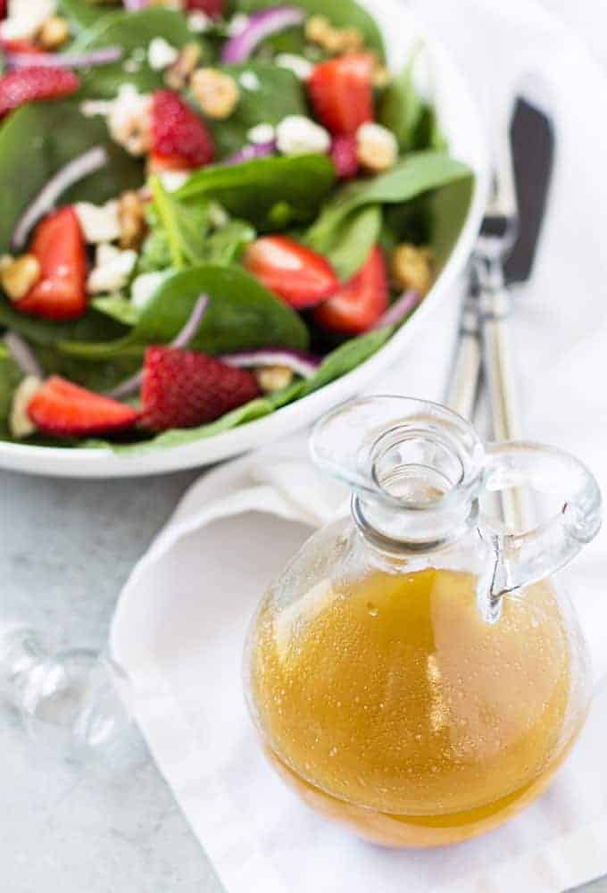 Angled overhead view of a clear bottle of vinaigrette. A salad is in the background.
