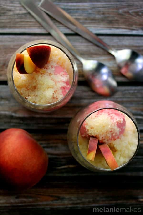 Overhead view of peach sundaes in glasses by two spoons on a wood surface.
