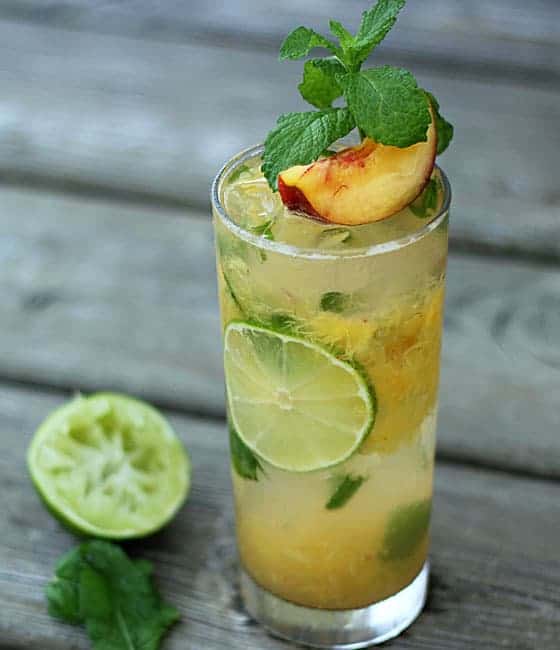 A peach mojito garnished with a fresh peach slice and mint on a wood surface.