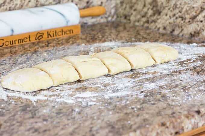 Dough that has been shaped into a rectangle and sliced into six sections on a floured granite surface.