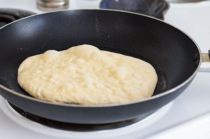 Naan flatbread dough being cooked in a skillet.