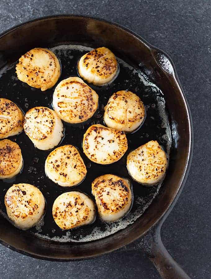 Overhead view of seared sea scallops in a cast iron skillet.