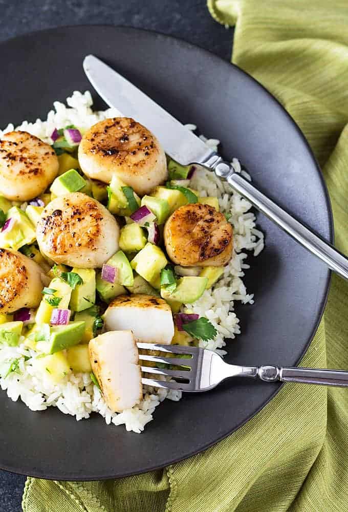 Overhead view of seared sea scallops with pineapple salsa over rice on a black plate.