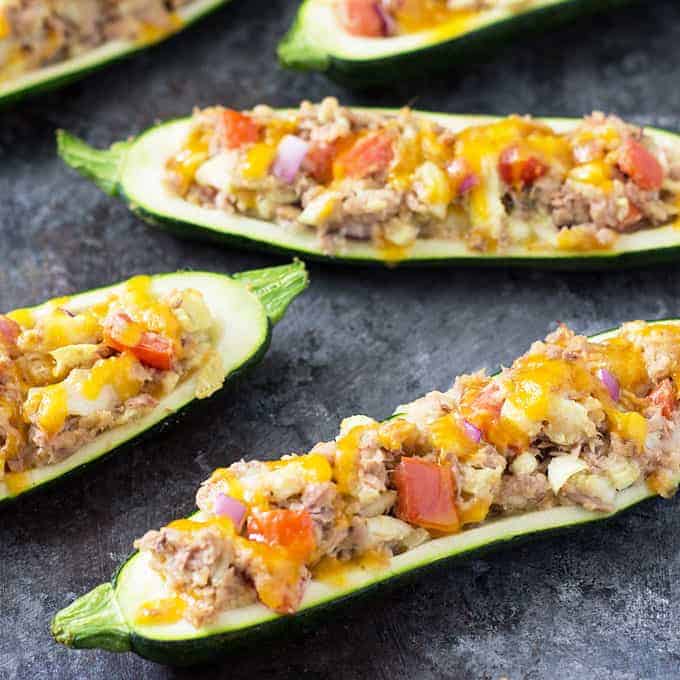Closeup view of tuna and vegetable zucchini boats on a dark surface.