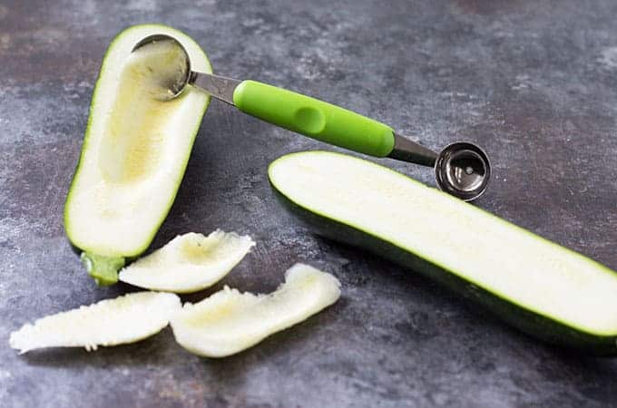 Removing pulp from a zucchini that has been sliced in half lengthwise with a melon baller.