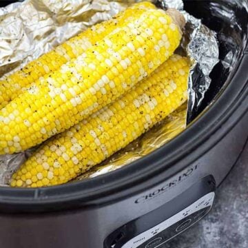 Three ears of corn on the cob in a slow cooker with aluminum foil.