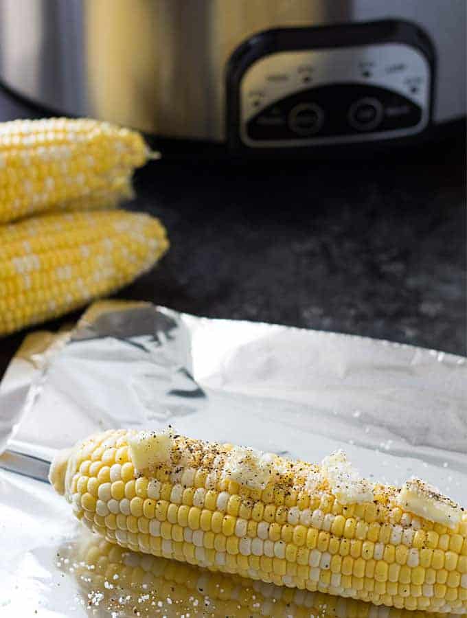 An ear of raw corn topped with butter on a piece of aluminum foil.