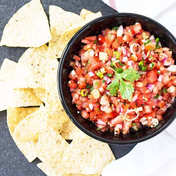 Overhead view of salsa in a black bowl garnished with a sprig of cilantro beside chips.