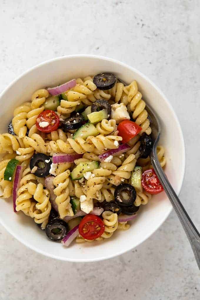 Overhead closeup view of Greek pasta salad in a round white bowl with a fork.