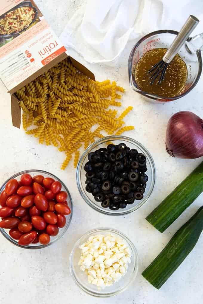 Overhead view of spiral pasta, vinaigrette dressing, vegetables, feta and black olives.