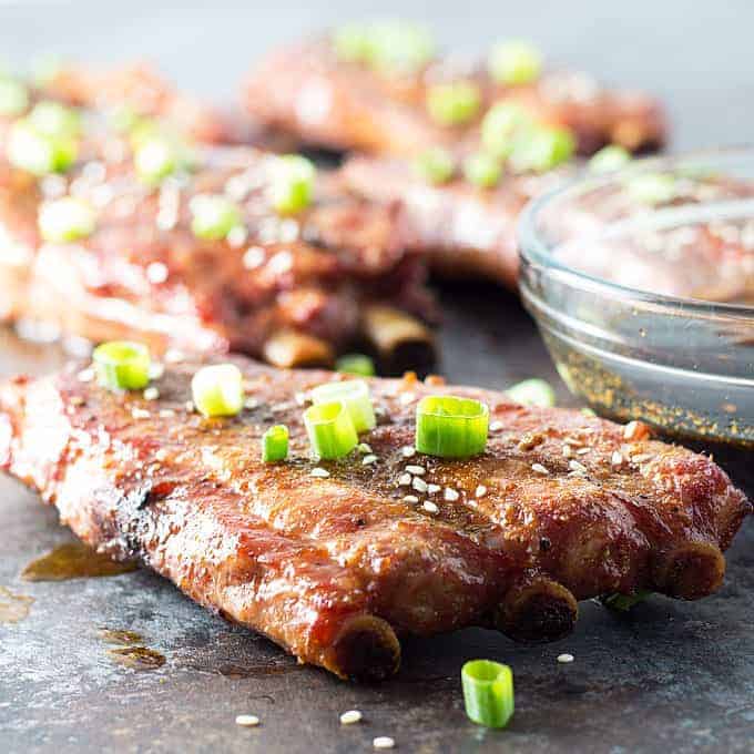 Front view of grilled ribs topped with sliced green onions by a bowl of sauce.