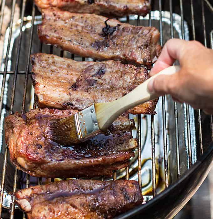 Brushing sauce on ribs on a grill with a basting brush.