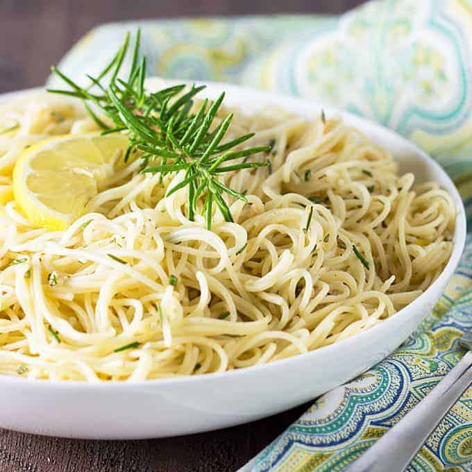 Front closeup view of lemon garlic pasta in a white bowl by a patterned napkin.