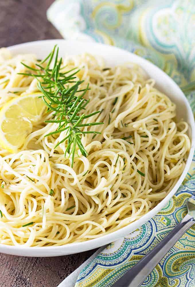 Closeup view of angel hair pasta garnished with lemon and rosemary in a white bowl.