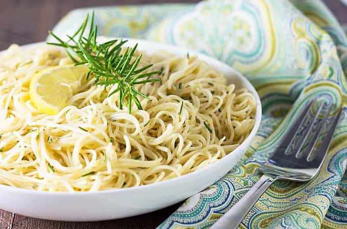 Front closeup view of lemon pasta in a white bowl by a fork and a patterned napkin.