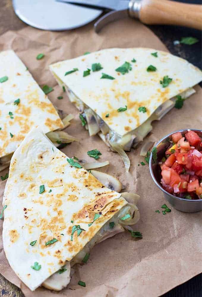 Three triangle slices of quesadillas on brown paper with a small cup of salsa.
