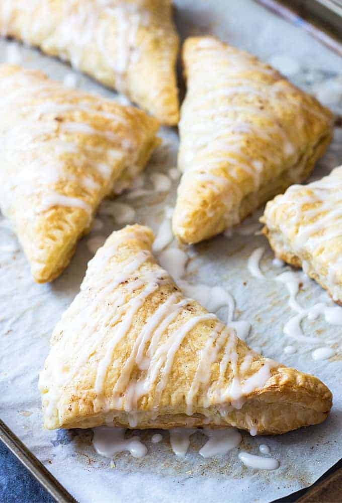 Apple turnovers prepared with puff pastry on a baking sheet lined with parchment paper.