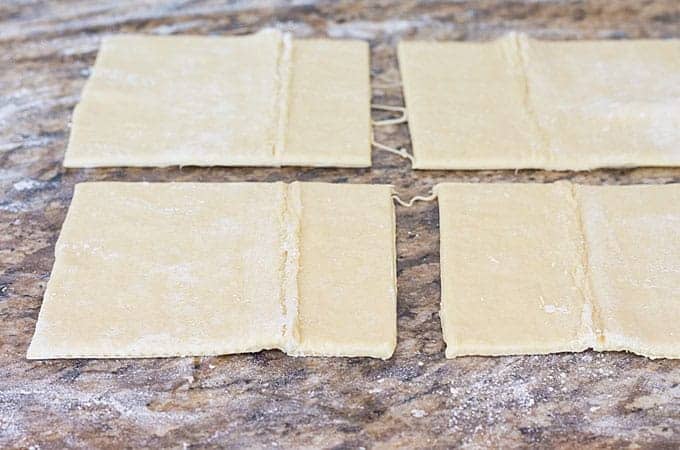 A puff pastry sheet sliced into four even squares on a floured surface.