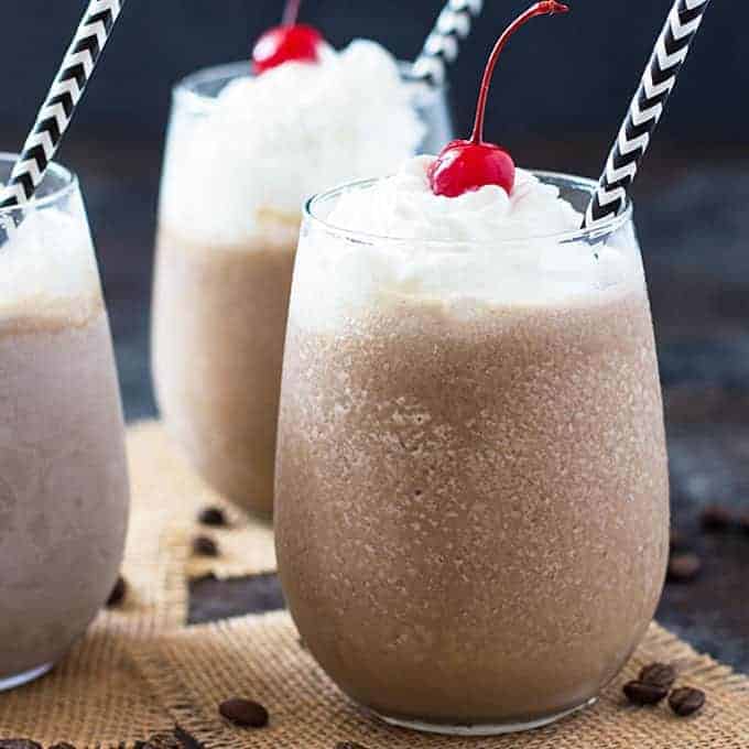 Front closeup view of three frozen coffee cocktails topped with whipped topping maraschino cherries.