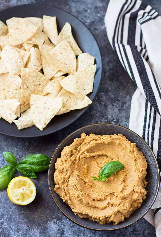 Overhead view of a bowl of hummus by a plate of tortilla chips and a kitchen towel.