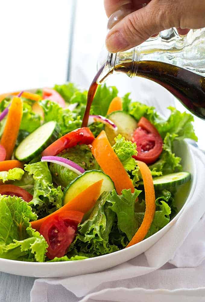 Pouring balsamic vinaigrette on a garden salad in a white bowl.