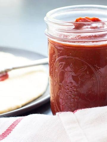 Homemade pizza sauce in a Mason jar in front of pizza dough
