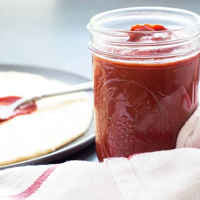 Closeup view of a jar of sauce.  Pizza dough in a pan is in the background.