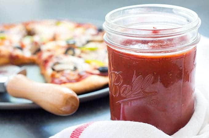 Closeup view of pizza sauce in a jar.  A cooked pizza is in the background.