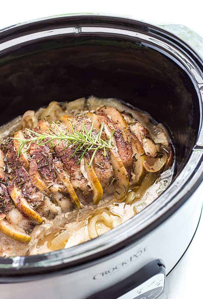 A sliced cooked pork loin with sliced apples stuffed in the slices in a slow cooker.