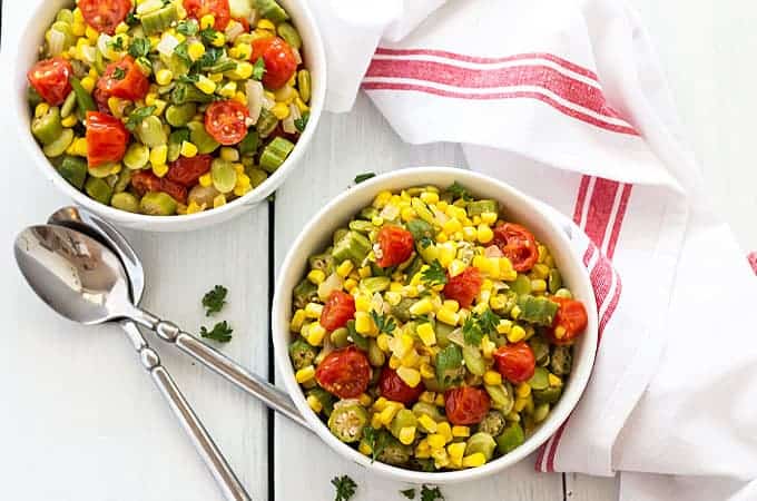 Overhead view of two white bowls of summer vegetable succotash by two spoons.