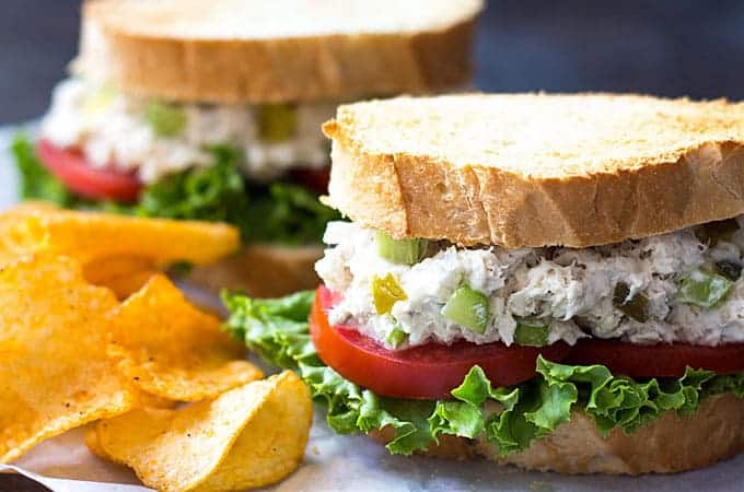 Front closeup view of a fish salad sandwich with lettuce and tomato by potato chips.