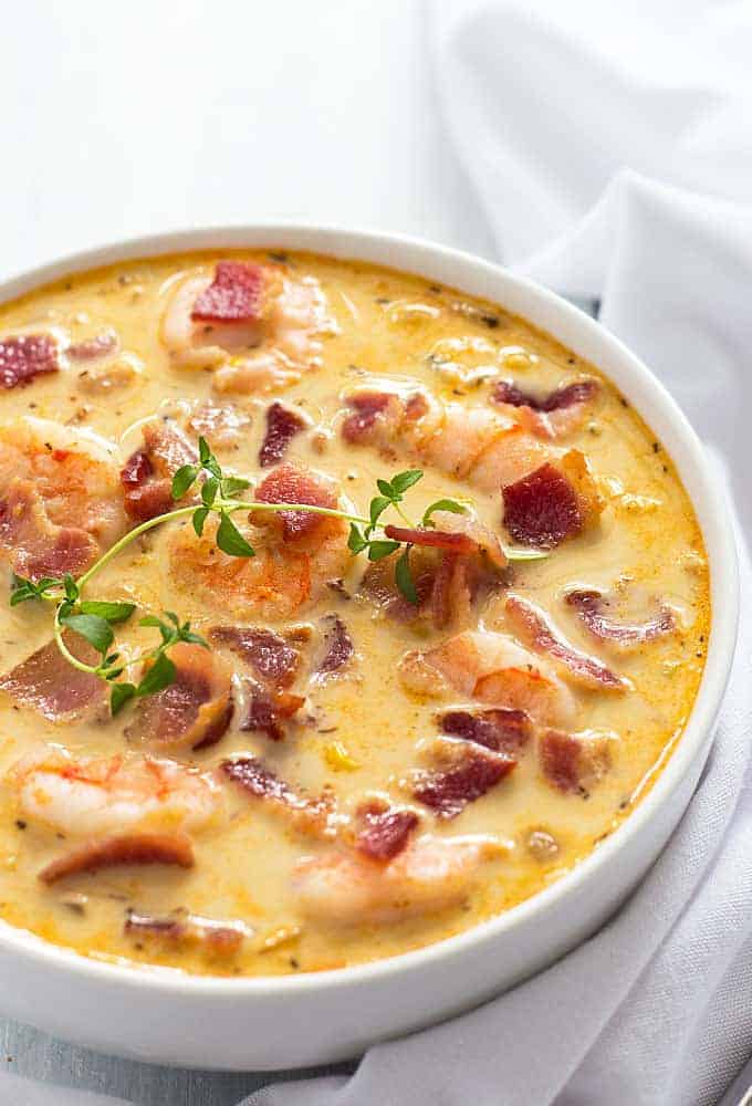 Closeup view of a white bowl of shrimp and corn chowder with bacon beside a white napkin.