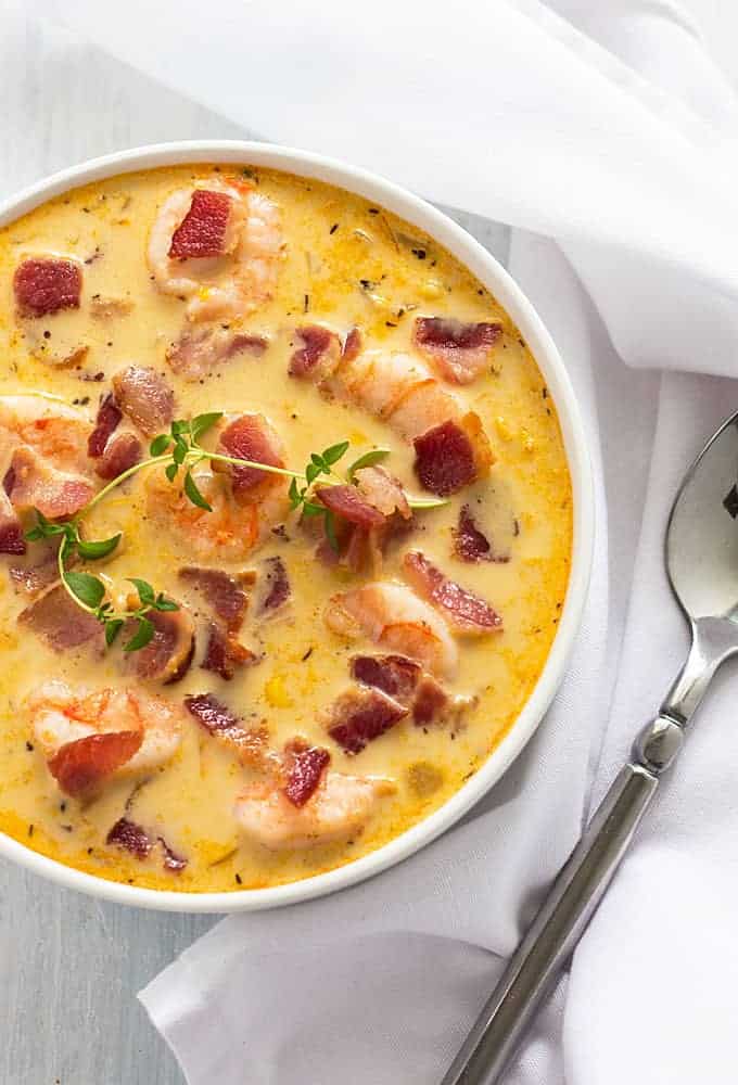 Overhead view of a white bowl of bacon, shrimp and corn chowder by a spoon.