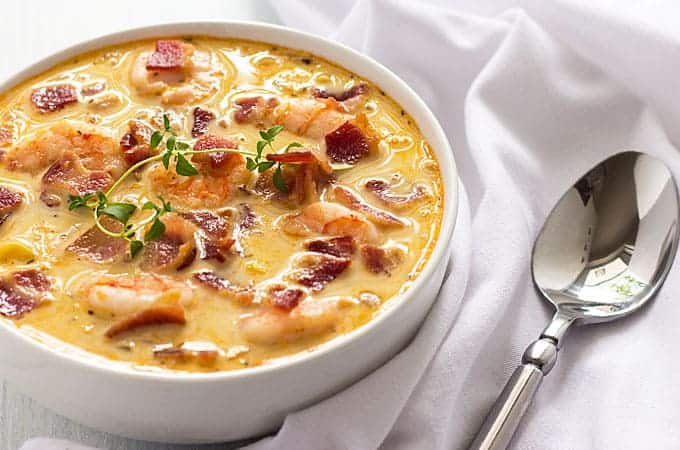 Chowder with bacon, shrimp and corn topped with a sprig of fresh thyme in a white bowl.