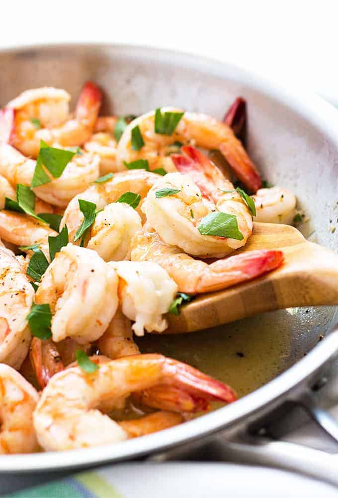Closeup view of shrimp in a garlic butter sauce in a skillet with a wooden spoon.