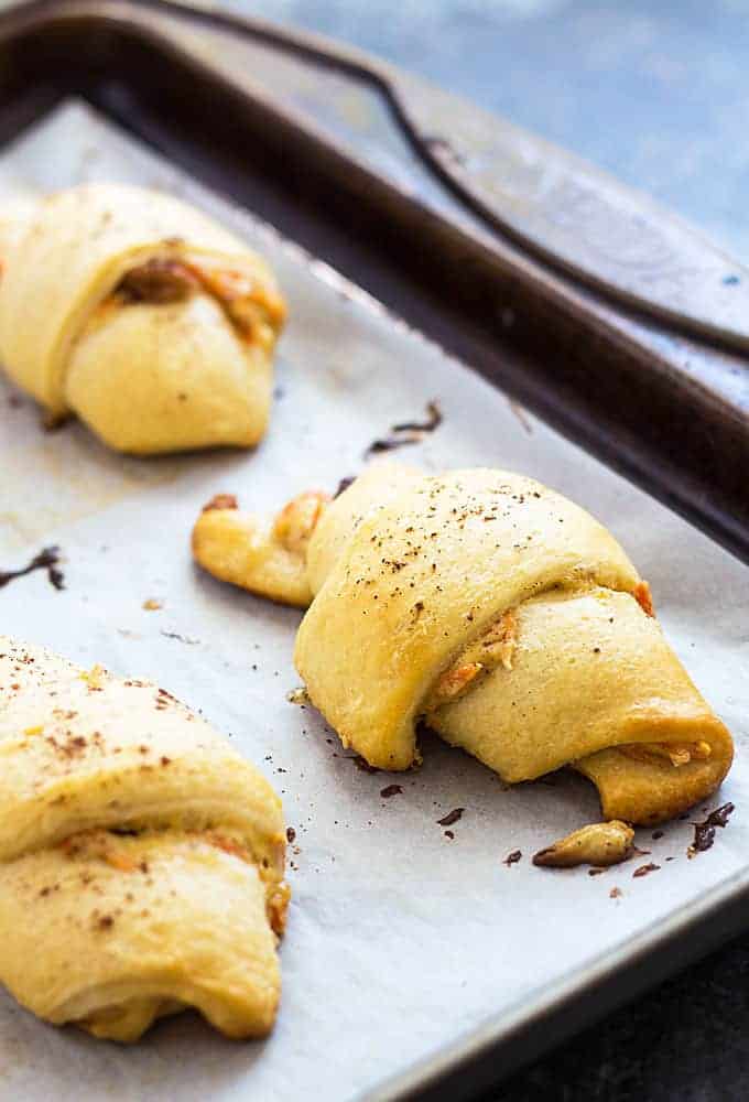 Closeup view of baked carrot crescent rolls on a baking sheet lined with parchment paper.