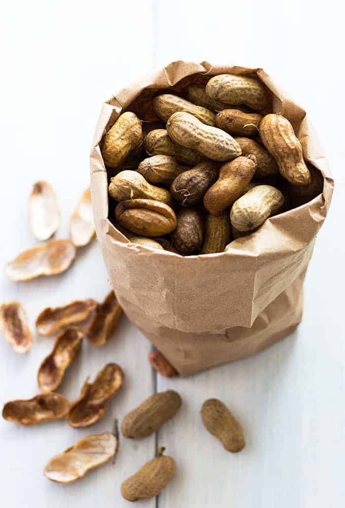 A small brown paper bag filled with boiled peanuts on a white surface.