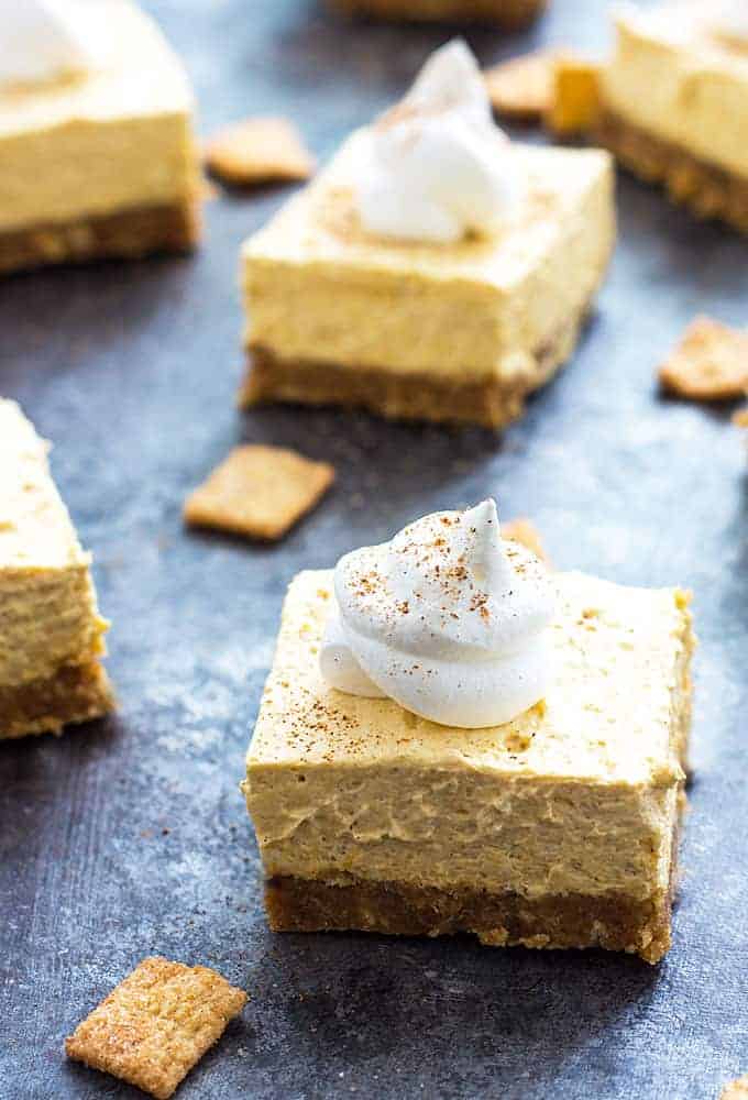 Pumpkin cheesecake bars topped with whipped topping on a dark surface.
