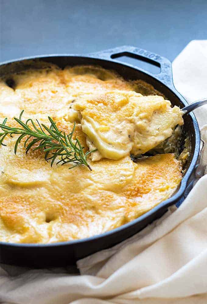 Front view of au gratin potatoes in a cast iron skillet being spooned out with a serving spoon.