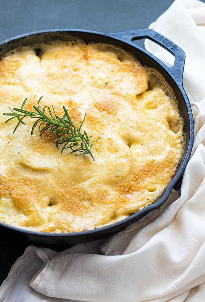Overhead view of Parmesan au gratin potatoes in a skillet topped with a rosemary sprig.