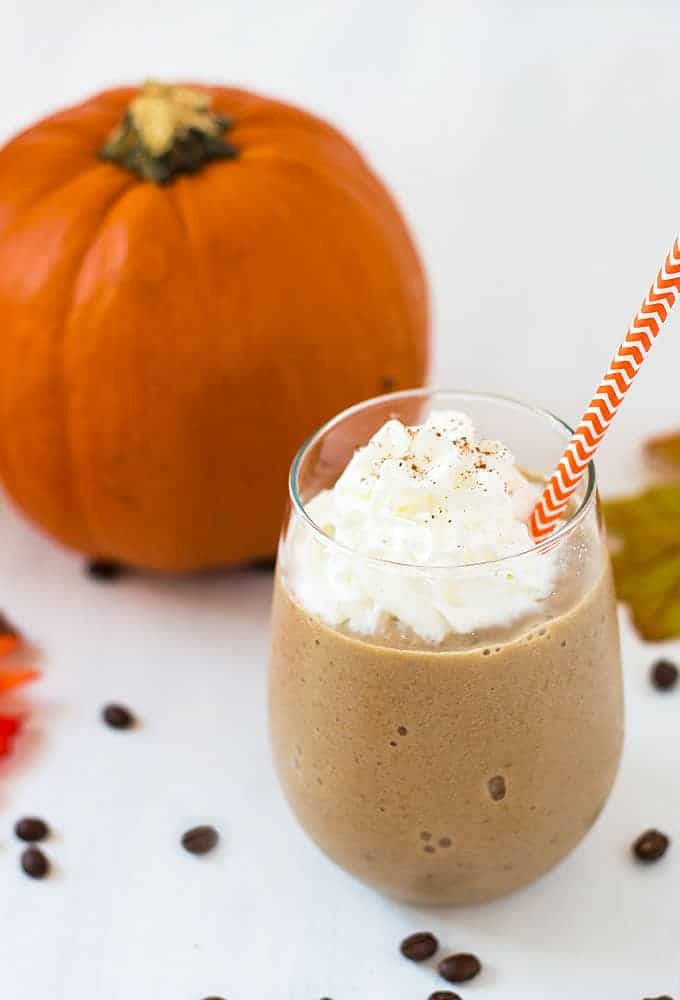 A frozen coffee smoothie in a glass with a straw.  A pumpkin is in the background.