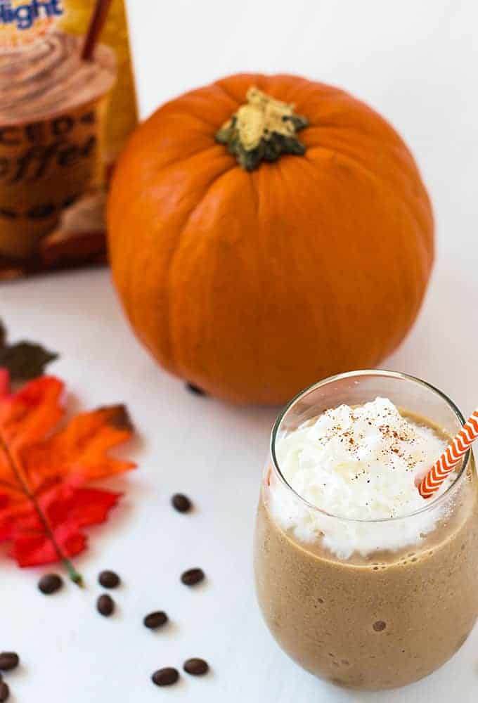 Overhead view of a frozen smoothie beside a pumpkin on a white surface with coffee beans.
