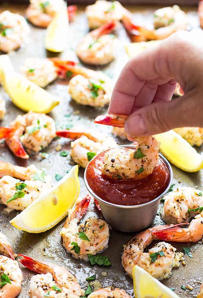 A hand holding and dipping a shrimp into a sauce cup of cocktail sauce.