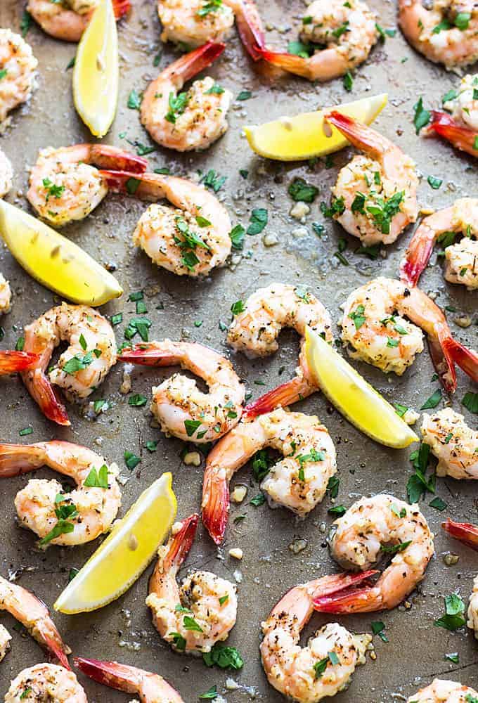 Overhead closeup view of roasted garlic shrimp on a baking sheet with lemon wedges.