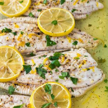 A closeup of baked flounder fillets in a baking dish with sliced lemons.